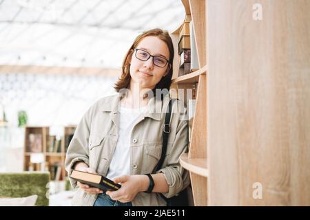 Junge Brünette Teenager Mädchen Student in Brille mit Handy in der modernen Bibliothek, öffentlichen Ort Stockfoto