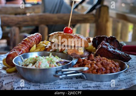 Teller mit Burger, Rippchen und Schweinefleisch mit verschiedenen Salaten auf rustikalem Tisch Stockfoto