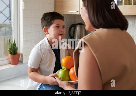 Kleiner Junge, der der Mutter eine Schale mit frischen Früchten gab, wusch er sie Stockfoto