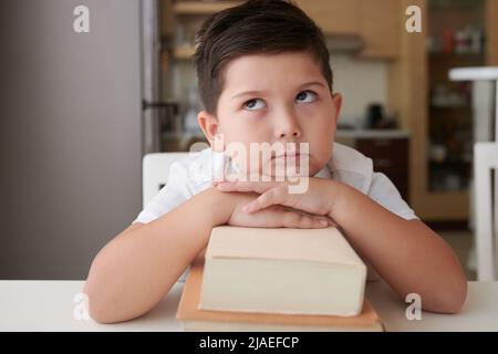 Nachdenklich niedlichen kleinen Jungen lehnt sich auf Stapel von Büchern und suchen nach oben Stockfoto