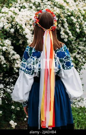 Das Mädchen steht mit dem Rücken in ukrainischer Nationalkleidung und einem Kranz mit Bändern auf dem Kopf. Stockfoto