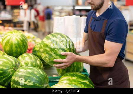 Nicht erkennbarer Supermarktarbeiter, der Uniform trägt und frische Wassermelonen auslegt, Platz zum Kopieren Stockfoto