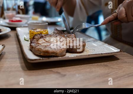 Nahaufnahme Teilansicht der Frau, die gerne Steak mit Gabel und Messer im Restaurant isst Stockfoto