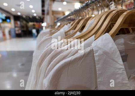 Weiße Kleidung hängt an Holzregalen. Kleidung für Frauen, die an Kleiderbügeln in einem Einkaufszentrum hängen, zum Verkauf. Stockfoto