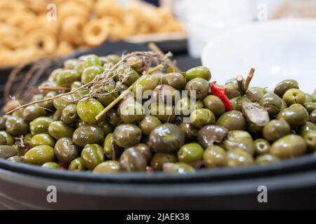 Grün zerkleinerte marinierte Oliven. Köstliche eingelegte Snack angezeigt Plastikkorb Stockfoto