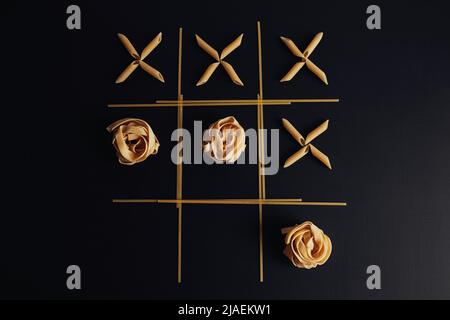 Top-Down-Ansicht von Tic Tac Toe Game mit verschiedenen Arten von Pasta auf dem schwarzen Hintergrund ausgelegt Stockfoto