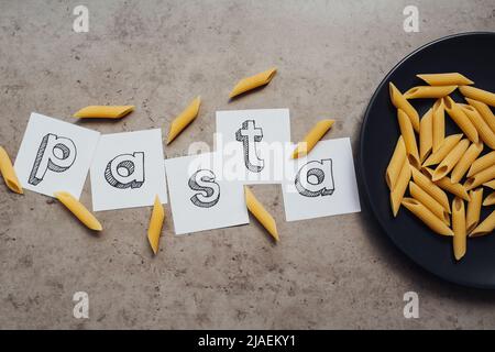 Schriftzug mit einer Handvoll Pasta auf dem schwarzen Teller auf dem Tisch Stockfoto