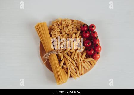 Verschiedene Arten von Pasta und Kirschtomaten auf dem Tablett auf dem weißen Hintergrundtisch Stockfoto