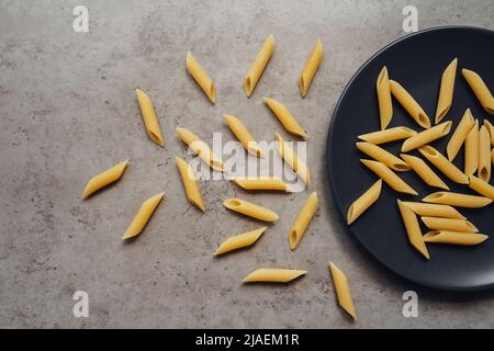 Eine Handvoll Pasta verstreut auf dem schwarzen Teller auf dem Tisch Stockfoto