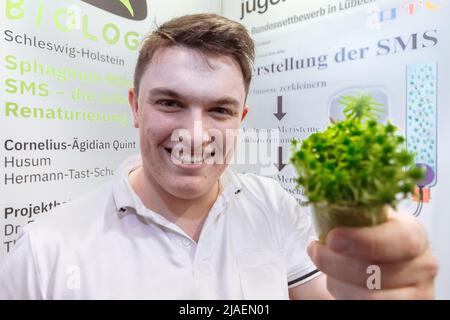 28. Mai 2022, Schleswig-Holstein, Lübeck: Cornelius-Ägidian Quint aus Schleswig-Holstein zeigt sein Forschungsobjekt MOSS beim Landesfinale von Jugend forscht 57.. Er entwickelte eine innovative Methode, die es Moosen ermöglicht, sich auf ehemaligen Moorgebieten schneller wieder zu etablieren, um sie zu renaturieren. Für das originellste Werk wurde ihm der Kanzlerpreis verliehen. Insgesamt 108 Forschungsprojekte nahmen am Landesfinale 57. von Jugend forscht Teil. Foto: Markus Scholz/dpa Stockfoto