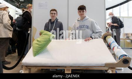 28. Mai 2022, Schleswig-Holstein, Lübeck: Ben Walter (l.) und Bendikt Wolf aus Bayern präsentieren beim "Jugend forscht"-Nationalfinale 57. ihr Aufwachbett. Gesteuert durch Smart-Home-Software entwickelten sie sich selbst, das Bett weckt den Schläfer mit einem Schüttelkissen, entfernt die Decke und "dustet" ihn am Ende hydraulisch. Insgesamt 108 Forschungsprojekte nahmen am Landesfinale von "Jugend forscht" 57. Teil. Foto: Markus Scholz/dpa Stockfoto