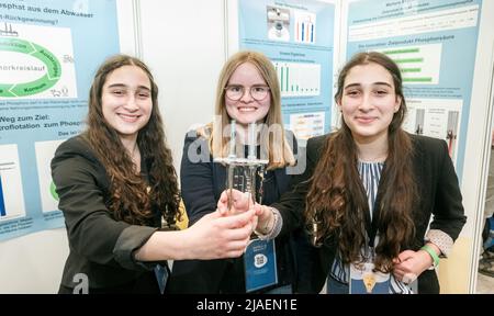 28. Mai 2022, Schleswig-Holstein, Lübeck: Lena Fries (l-r), Hannah Amrhein und Hanna Fries aus Bayern, die Chemie-Bundessiegerin von Jugend forscht, halten ihr Forschungstool, einen Becher mit Elektroden, in der Hand. Sie haben einen neuen Ansatz gefunden, um den Pflanzennährstoff Phosphor aus dem Abwasser zu recyceln. Insgesamt nahmen 108 Forschungsprojekte am nationalen Finale von „Jugend forscht“ 57. Teil. Foto: Markus Scholz/dpa Stockfoto