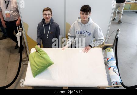28. Mai 2022, Schleswig-Holstein, Lübeck: Ben Walter (l.) und Bendikt Wolf aus Bayern präsentieren beim "Jugend forscht"-Nationalfinale 57. ihr Aufwachbett. Gesteuert durch Smart-Home-Software, die sie selbst entwickelt haben, weckt das Bett den Schläfer mit einem Schüttelkissen, entfernt die Decke und „duckt“ den Schläfer am Ende hydraulisch. Insgesamt 108 Forschungsprojekte nahmen am Landesfinale von „Jugend forscht“ 57. Teil. Foto: Markus Scholz/dpa Stockfoto