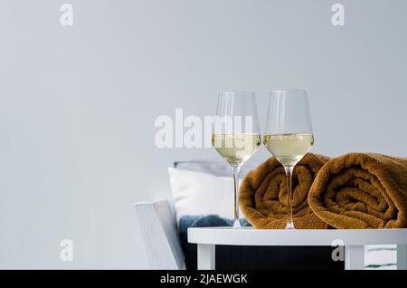 Zwei Gläser Weißwein auf einem Holztisch mit Poolhandtuch, um am Pool zu trinken. Stockfoto