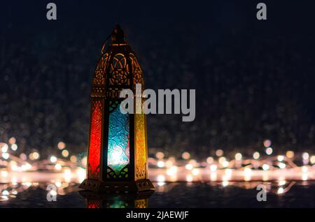 Laterne mit Lichtern, die für das islamische Neujahr dekoriert sind, am Fenster mit einem Regentropfen im Hintergrund. Stockfoto