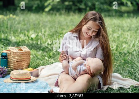 Neugeborenes verbringt Zeit draußen. Glückliche und lächelnde Mutter mit ihrem neugeborenen Baby, das Zeit im Park verbringt. Frische Luft und natürliches Sonnenlicht Stockfoto