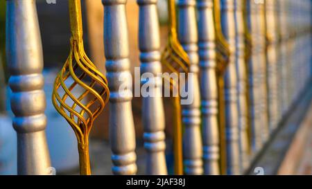 Schöner dekorativer schmiedeeiserer Zaun aus Gussmetall mit kunstvollem Schmieden. Eiserne Leitplanke aus nächster Nähe. Nahaufnahme des Zauns aus goldenem Chrom-Silber. Stockfoto