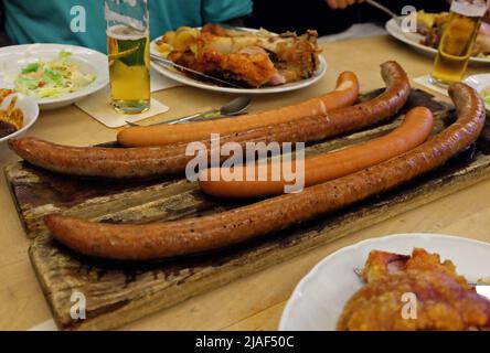 Nahaufnahme von deutschen Würstchen und frittierten Schweinerücken, serviert mit Eisbier, Krautsalat und verschiedenen Dip-Saucen Stockfoto