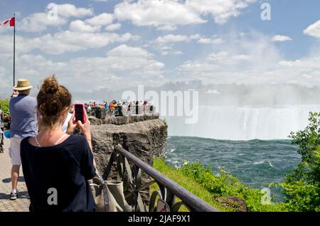 Frau, die ein Foto von den Niagarafällen mit ihrem Handy von der kanadischen Seite in Niagara Falls, Ontario, Kanada, macht Stockfoto