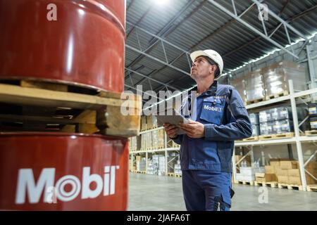 Jule 21, 2021 Chabarowsk, Russland: Ein Arbeiter in Overalls und ein Helm in einem Lager überprüft die in Fässern gelagerten Produkte. Stockfoto