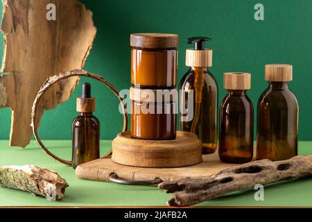 Braune Glasbehälter für Kosmetika mit Holzdeckeln. Cremedose, Tropfflasche und Lotion. Grüner Hintergrund. Pflege und Schönheit. Flaschen. Umweltfreundliches Konzept. Kosmetische Set-Box. Pipette und Spender. Stockfoto