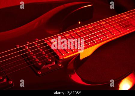 Schwarze E-Gitarre mit rotem Licht beleuchtet Stockfoto