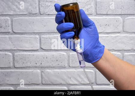 Medizinischer Tropfer und Arzthand in einem Handschuh vor dem Hintergrund der Wand Stockfoto