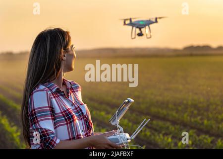 Hübsche junge Bäuerin, die im Frühjahr am Abend im Sojabohnenfeld mit Fernbedienung vor dem Traktor fährt Stockfoto