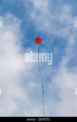 Ein leuchtender roter Drachen mit einem langen Schwanz, der hoch am blauen Himmel mit weißen Wolken fliegt Stockfoto