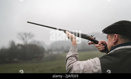 Hunter Mann in traditionellen Schießkleidung auf dem Feld mit Schrotflinte zielen. Stockfoto