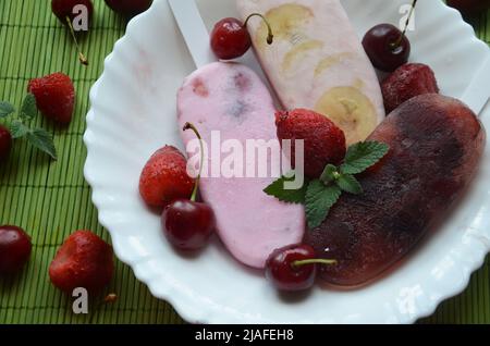 Hausgemachtes Erdbeer Kirsche Banane Heidelbeere Eis oder Eis Eis mit grünen Minze Blätter auf teal rustikalen Tisch, gefrorenen Fruchtsaft, Vintage-Stil dekoriert Stockfoto