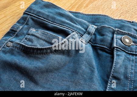 Nahaufnahme der Tasche und der Knopfansicht von hellblauem Jeans-Denim auf Holzboden Stockfoto