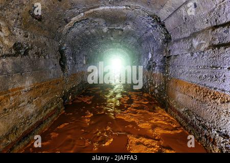 Dunkler, schmutziger, überfluteter, gewölbter Betonentwässerungsminentunnel Stockfoto