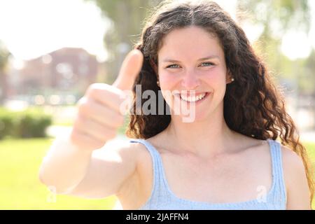 Vorderansicht Porträt einer glücklichen Frau, die einen sonnigen Tag in einem Park mit dem Daumen nach oben zeigt Stockfoto