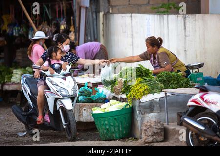 Luang Prabang, Laos - 15. November 2017: Eine nicht identifizierte Frau mit Gesichtsmaske kauft Gemüse von einem Straßenverkäufer in Luang Prabang, Laos. Stockfoto