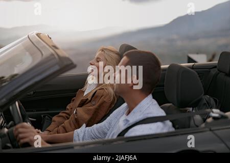 Fröhliches junges Paar, Mann und Frau in einem Cabriolet, die die Hände halten und sich glücklich fühlen Stockfoto