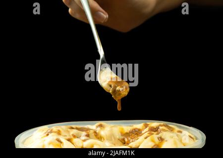Makrofoto eines Dessertlöffels mit Karamell-Eis über einem Eisbehälter vor einem schwarzen Hintergrund mit Kopierfläche. Stockfoto