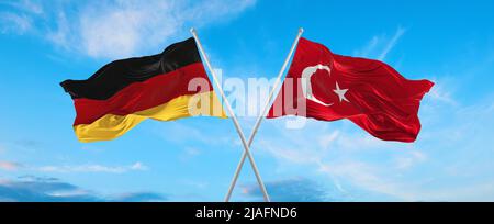 Zwei gekreuzte Flaggen Bundesrepublik Deutschland und Türkei winken im Wind bei bewölktem Himmel. Konzept von Beziehung, Dialog, Reisen zwischen zwei Countri Stockfoto