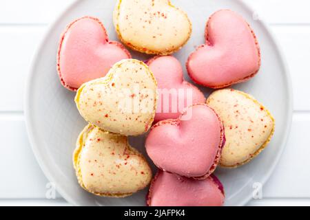 Herzförmig Süße Makronen auf dem Teller auf einem weißen Tisch. Draufsicht. Stockfoto