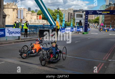 Zwei männliche behinderte Radfahrer, die auf rekumbanten Fahrrädern fahren und am RideLondon 2022 teilnehmen, halten sich nach dem Überqueren der Ziellinie auf der Tower Bridge in die Hände Stockfoto