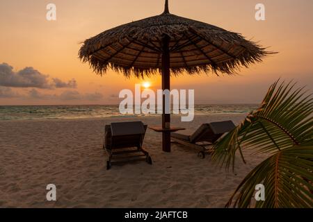 Schöner Panoramablick auf den Sonnenuntergang vom Ufer aus mit zwei Sonnenliegen und einem Strohschirm im Vordergrund. Beach Resort Erholungsurlaub Konz Stockfoto