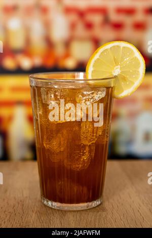 Glas mit Cola, Eis und Zitrone auf einer Holztheke vor einer Bar. Stockfoto