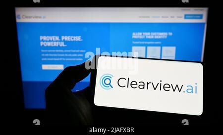 Person, die Mobiltelefon mit dem Logo des Gesichtserkennungsunternehmens Clearview AI Inc. Auf dem Bildschirm vor der Business-Webseite hält. Konzentrieren Sie sich auf die Telefonanzeige. Stockfoto