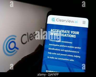 Person mit Smartphone und Webseite des Gesichtserkennungsunternehmens Clearview AI Inc. Auf dem Bildschirm mit Logo. Konzentrieren Sie sich auf die Mitte des Telefondisplays. Stockfoto