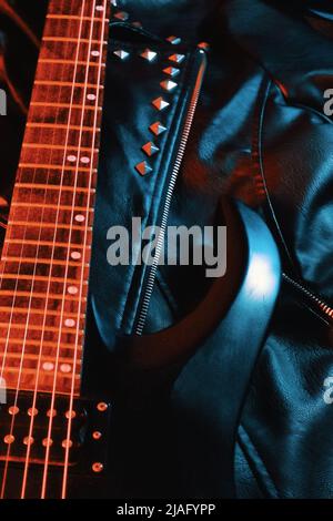 Schwarze E-Gitarre liegt auf einer Lederjacke Stockfoto