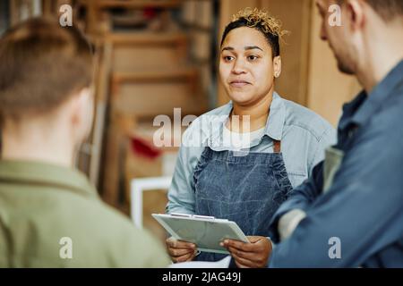 In warmen Farbtönen gehaltene Darstellung von weiblichen Handwerkerinnen, die in der Schreinerei Klienten beraten Stockfoto