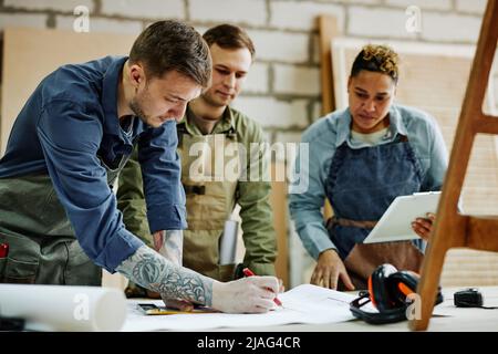 In warmen Farbtönen gehaltene Porträts moderner Handwerker, die in der Schreinerei über Möbelentwürfe diskutieren Stockfoto