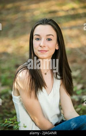 Ein schönes glückliches Teenager Brünette Mädchen im Freien auf einem Holzhackling sitzen und lächeln mit Kopierraum Stockfoto