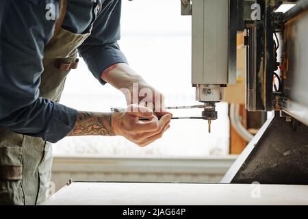 Seitenansicht Nahaufnahme eines tätowierten Arbeiters, der Maschineneinheiten in der Werkstatt repariert, Kopierraum Stockfoto