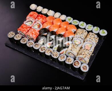 Große Auswahl an verschiedenen Sushi-Rollen mit frischen verschiedenen Füllungen auf einem schwarzen Steinteller. Stockfoto